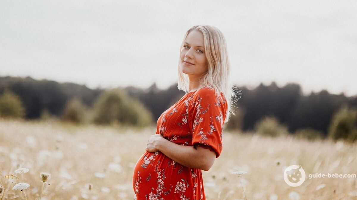 Femme enceinte en robe rouge à fleurs dans un champs